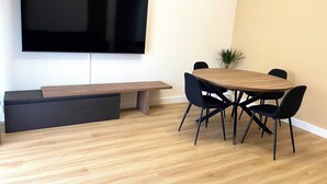 A modern room with a flat-screen TV mounted on the wall, a wooden bench, and a round table with chairs. - Rome Vatican/ Dimora 63 AIR CONDITIONING & WI-FI Premium Apartment (Roma)