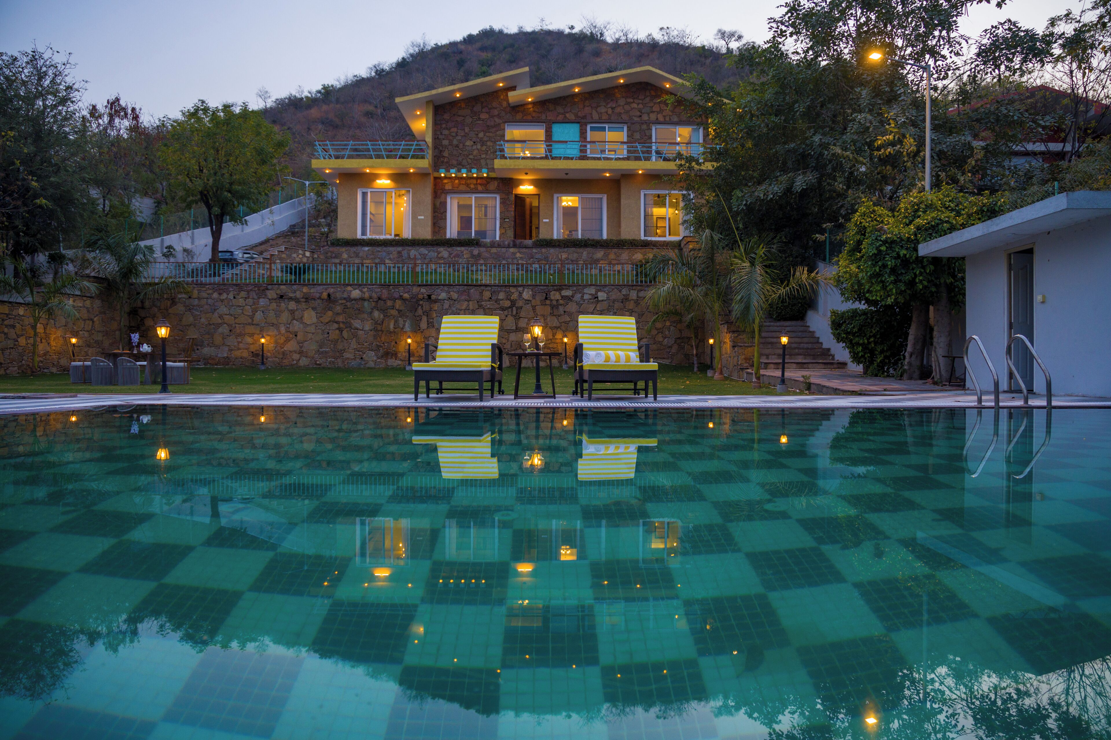 A pool with checkered tiles, two lounge chairs, and a building with multiple windows and balconies in the background.