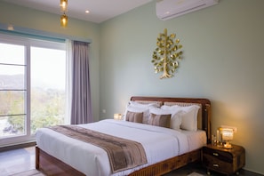 A bedroom with a large bed, a nightstand with a lamp, a wall-mounted tree decoration, and a window with curtains. - ELIVAAS Festiva Mansion 3 BHK Villa (Udaipur)