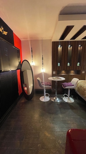 A modern room with a television, two chairs, a small table, and a bed.