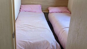 Um quarto pequeno e estreito com duas camas, cada uma com cabeceira de madeira e roupa de cama rosa.