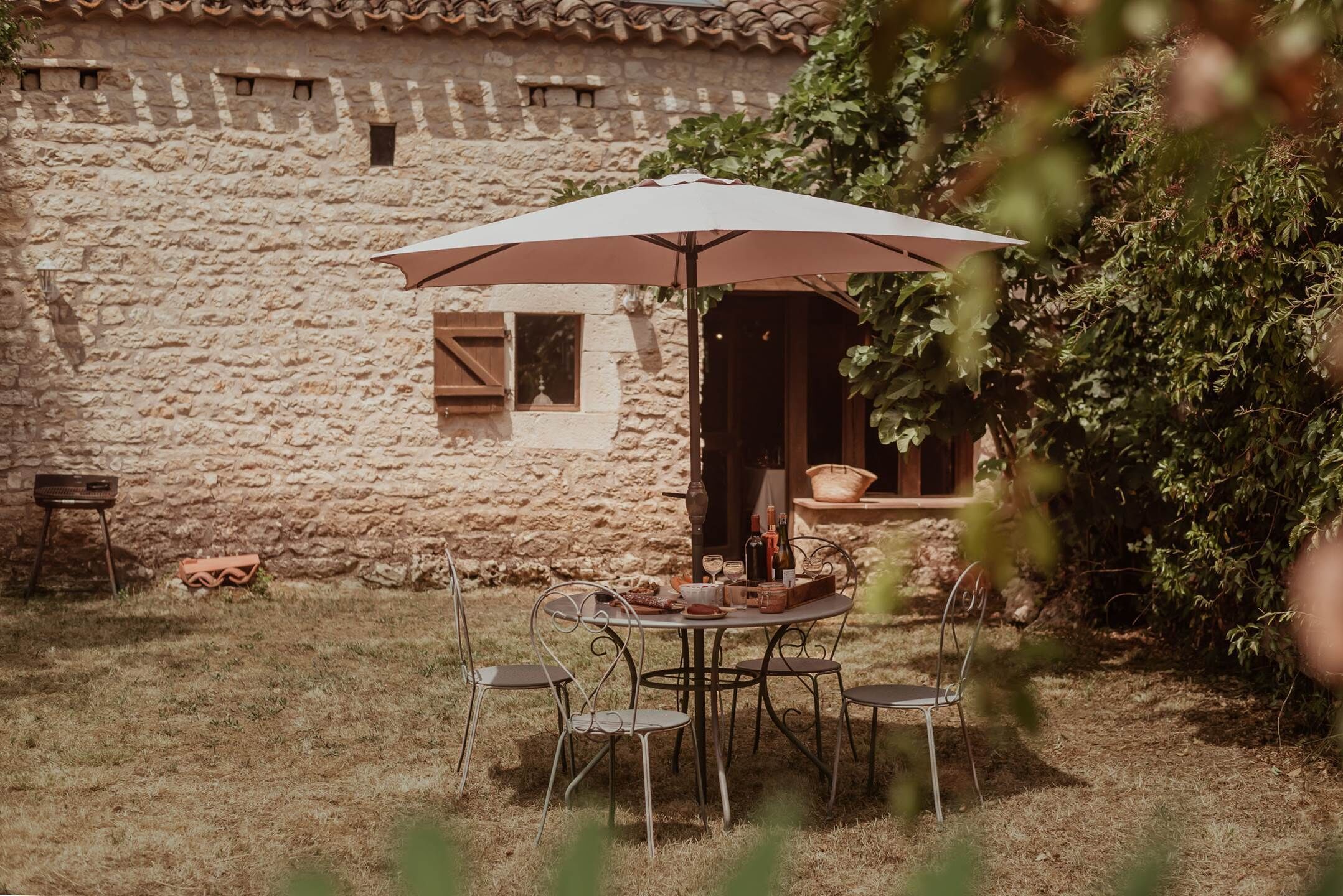 Een terras buiten met een stenen muur, een tafel met stoelen en een grote parasol.