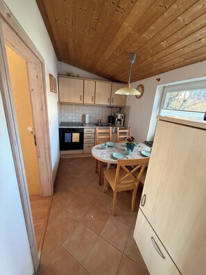A kitchen with wooden cabinets, a tiled backsplash, a round table with chairs, and a window with a view of trees. - Apartment 3 Geltinger Bucht - relaxation near the beach & nature (Gelting)