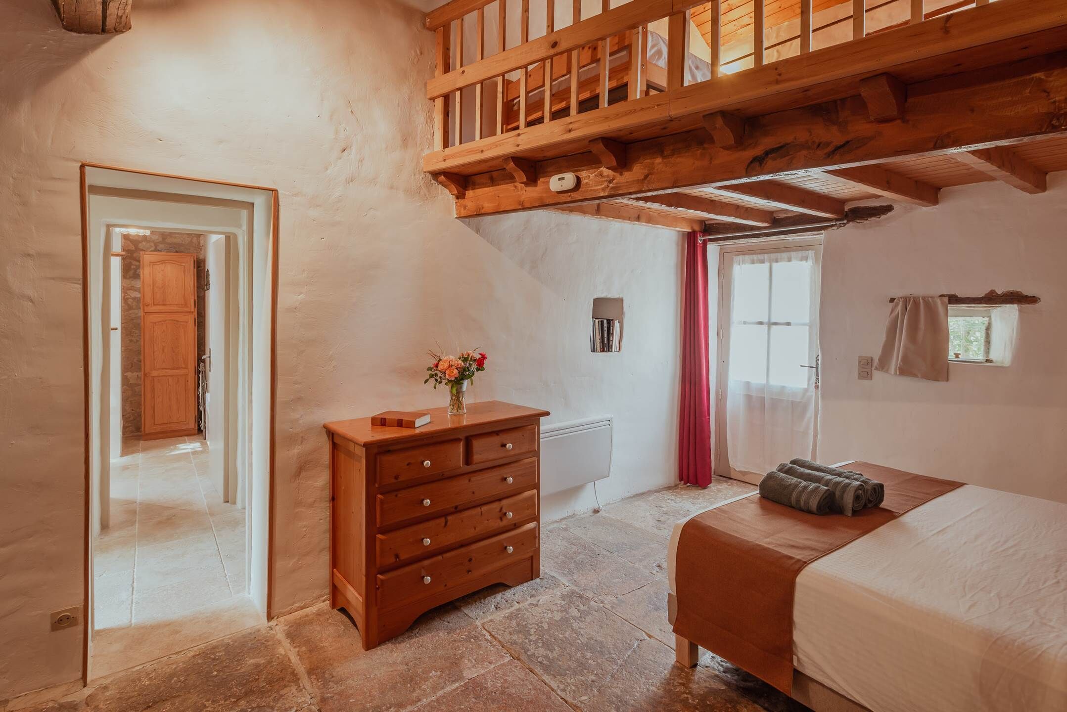 A bedroom with a wooden bed, a dresser, a mirror, and a door leading to another room.