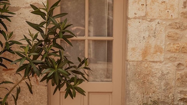 Un edificio in pietra con una porta beige, un piccolo gradino che conduce all'ingresso e un cesto di vimini a terra.