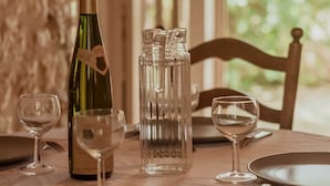 Un tavolo da pranzo apparecchiato con bicchieri da vino, una bottiglia e una caraffa, con una parete in pietra e una finestra sullo sfondo.