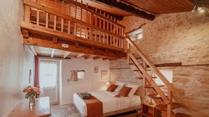 Una camera da letto con una scala in legno, un letto con cuscini, un comodino, un vaso con fiori e una parete in pietra.