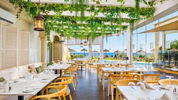 A restaurant with tables set for dining, a pool area, and a view of the sea. - AP Oriental Beach - Adults Only (Portimão)