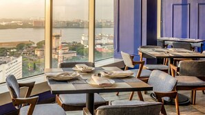 A restaurant with tables set for dining, a view of a river and buildings, and blue walls. - Suasana JB Central by TPL (Johor Bahru)