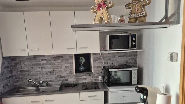 Una cucina moderna con mobili bianchi, zoccolo in pietra, forno a microonde integrato, macchina del caffè e una piccola isola con portascopino.