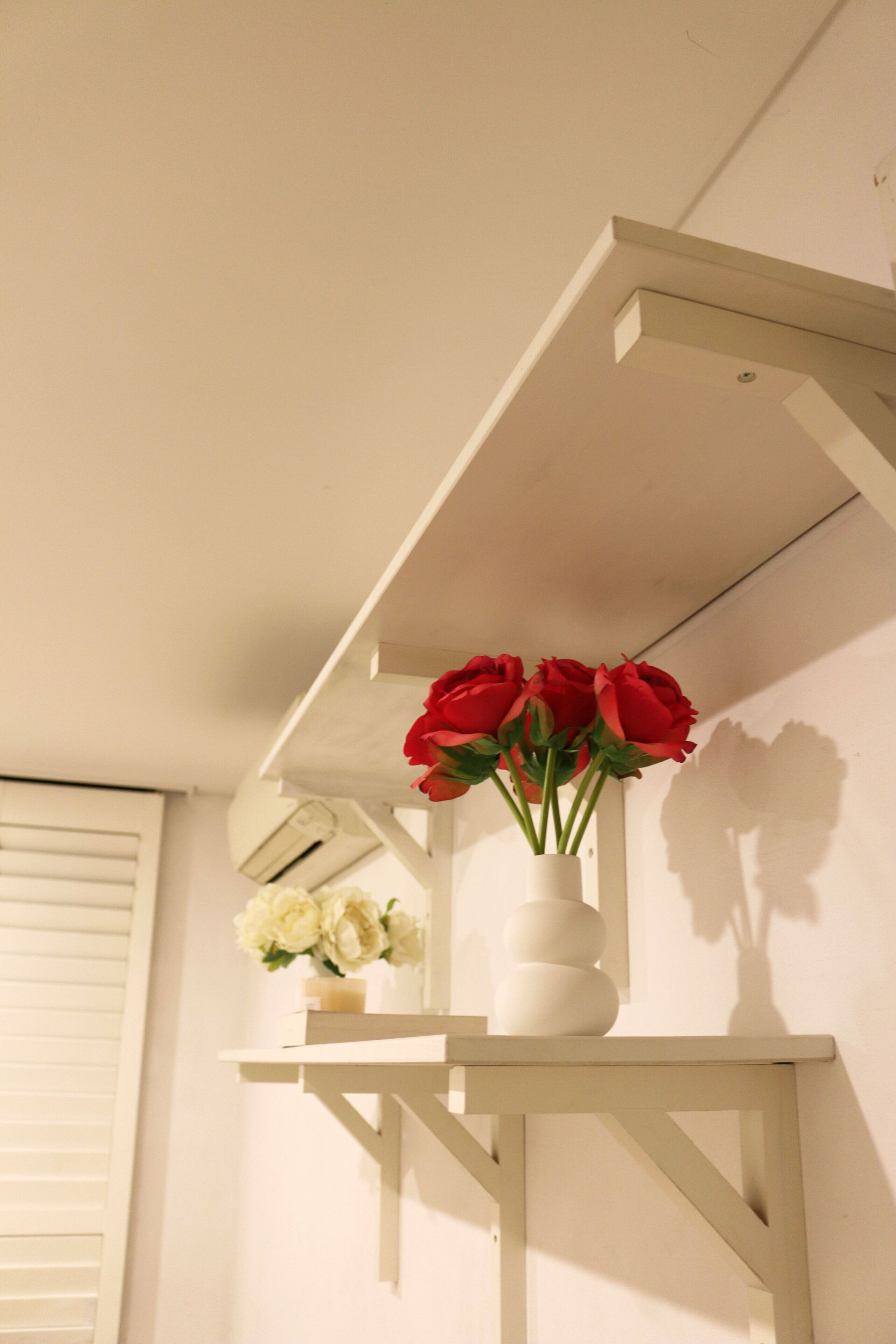A white shelf with a vase of red flowers and a smaller vase of white flowers.