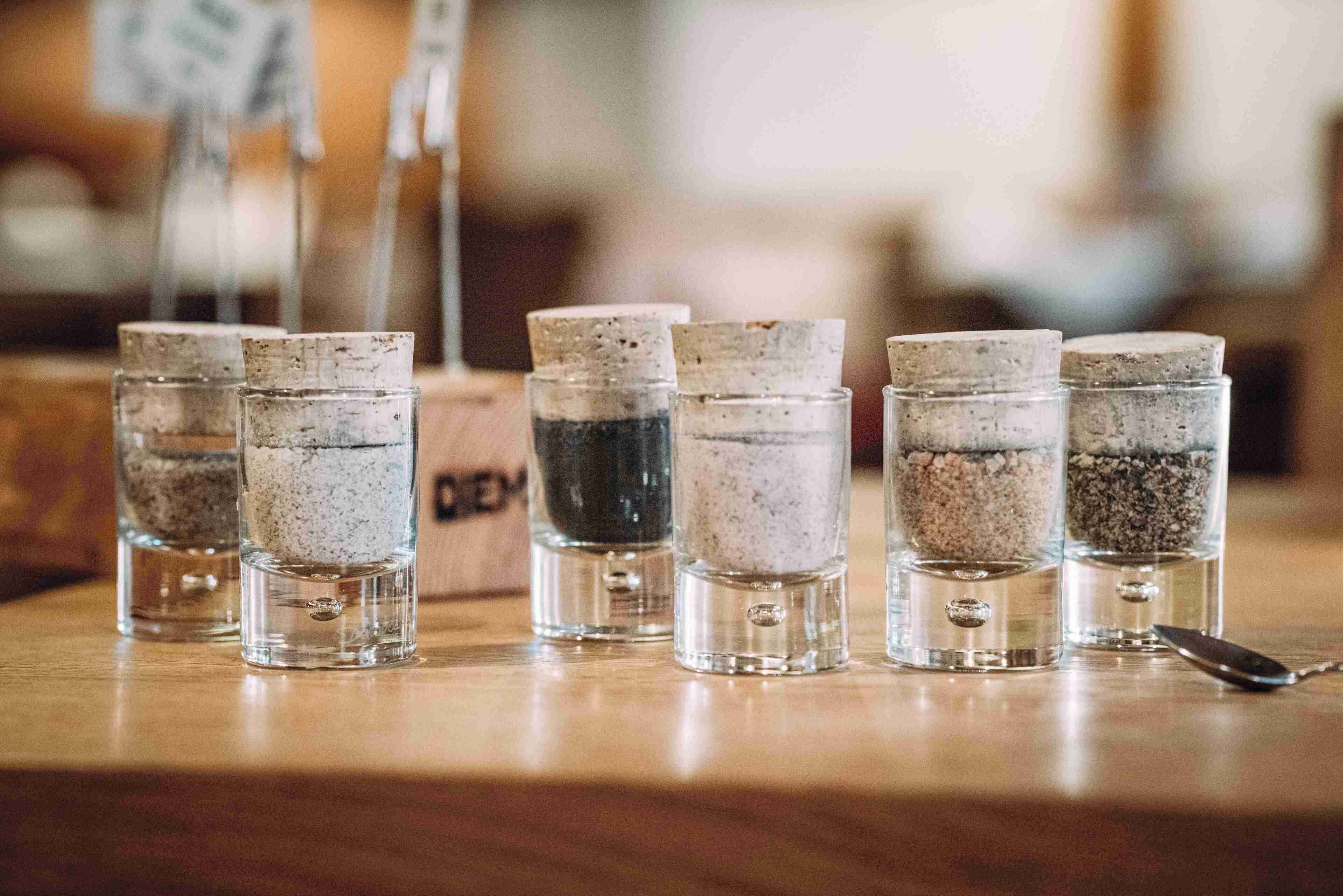 Une rangée de verres à shooter contenant différents liquides de couleurs variées, disposés sur une surface en bois.
