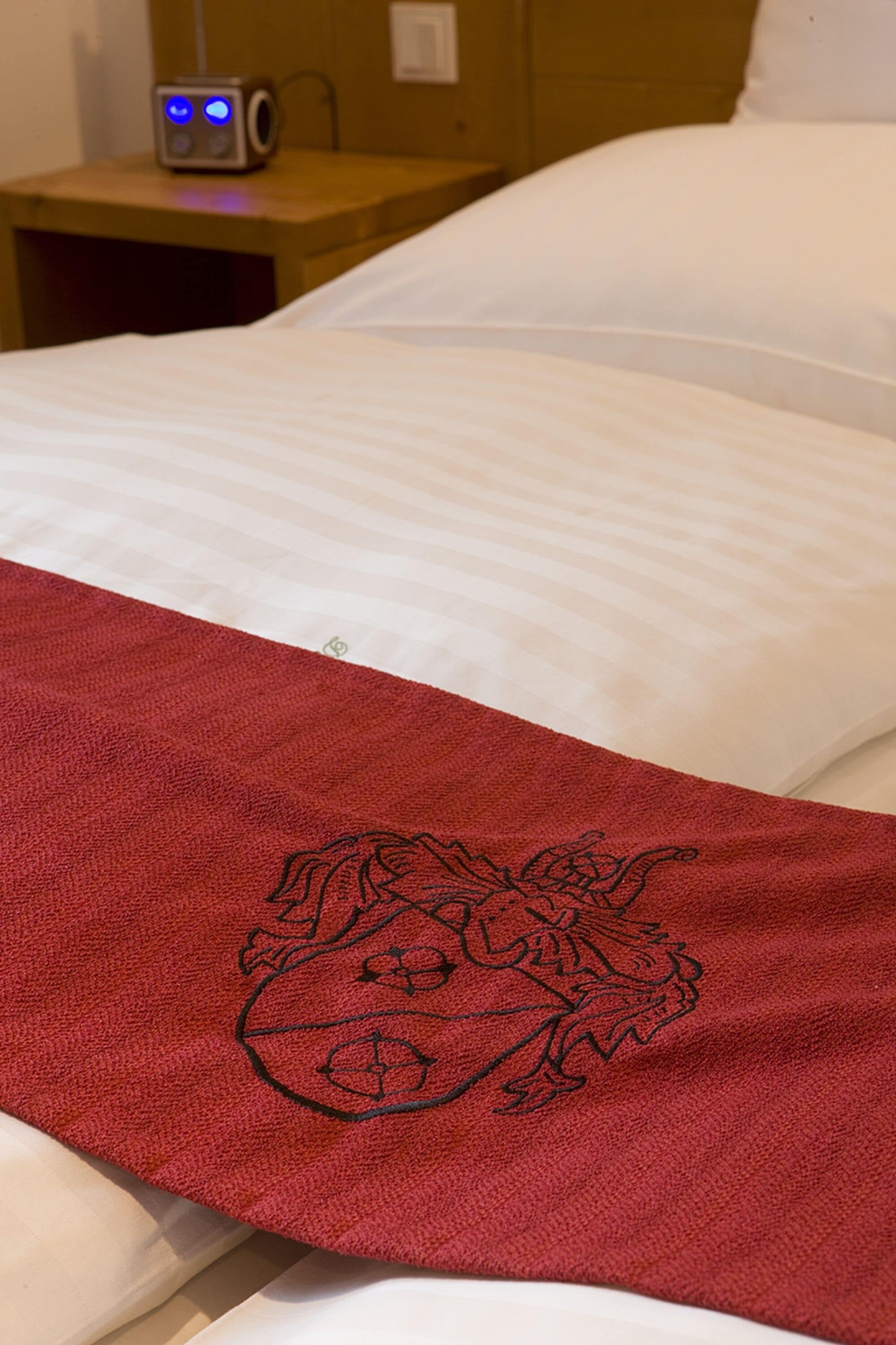 Un lit avec du linge de lit blanc et une serviette rouge ornée d’un motif floral.