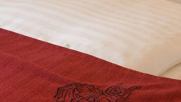 Un lit avec du linge de lit blanc et une serviette rouge ornée d’un motif floral.
