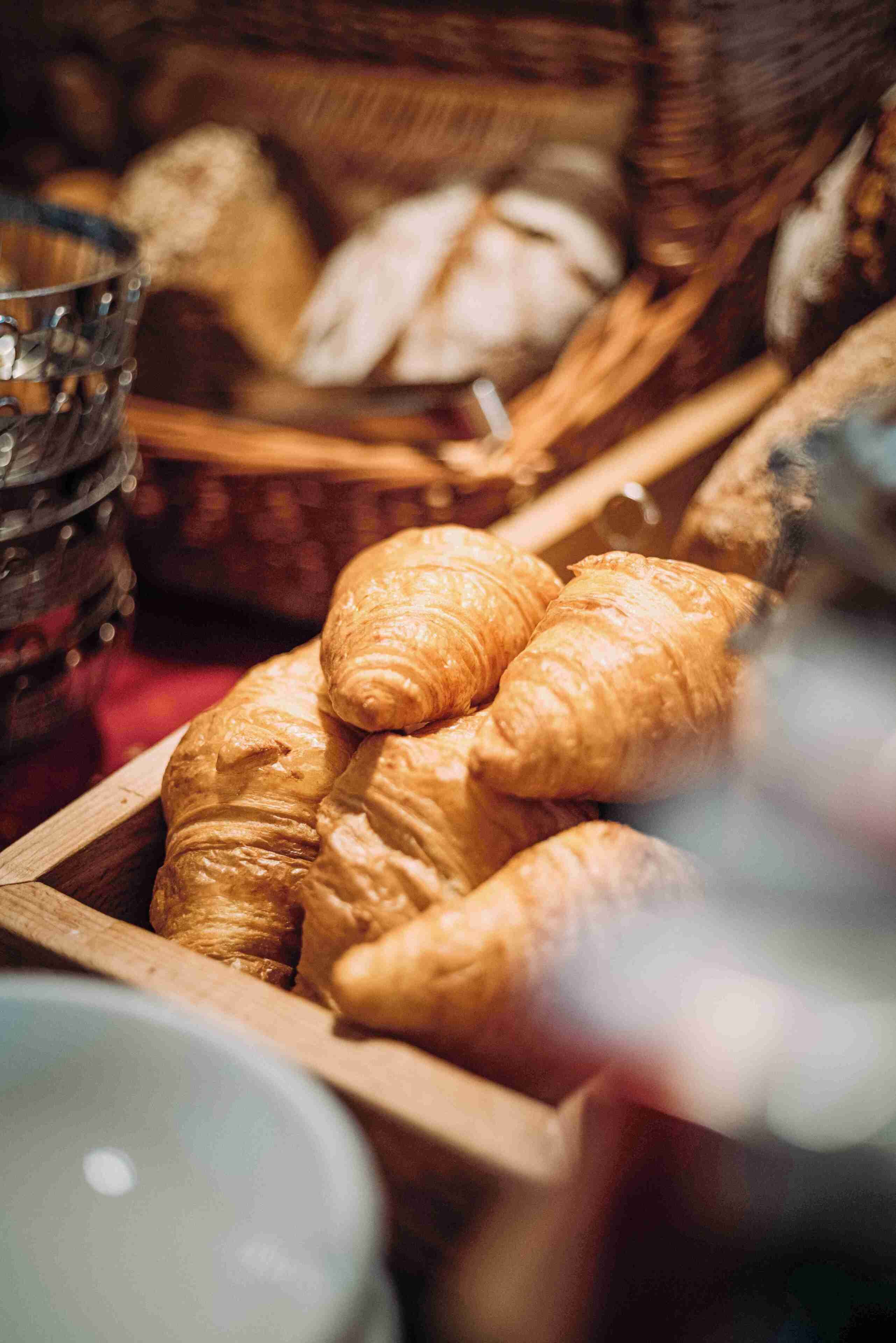 A wooden basket filled with croissants and other baked goods.