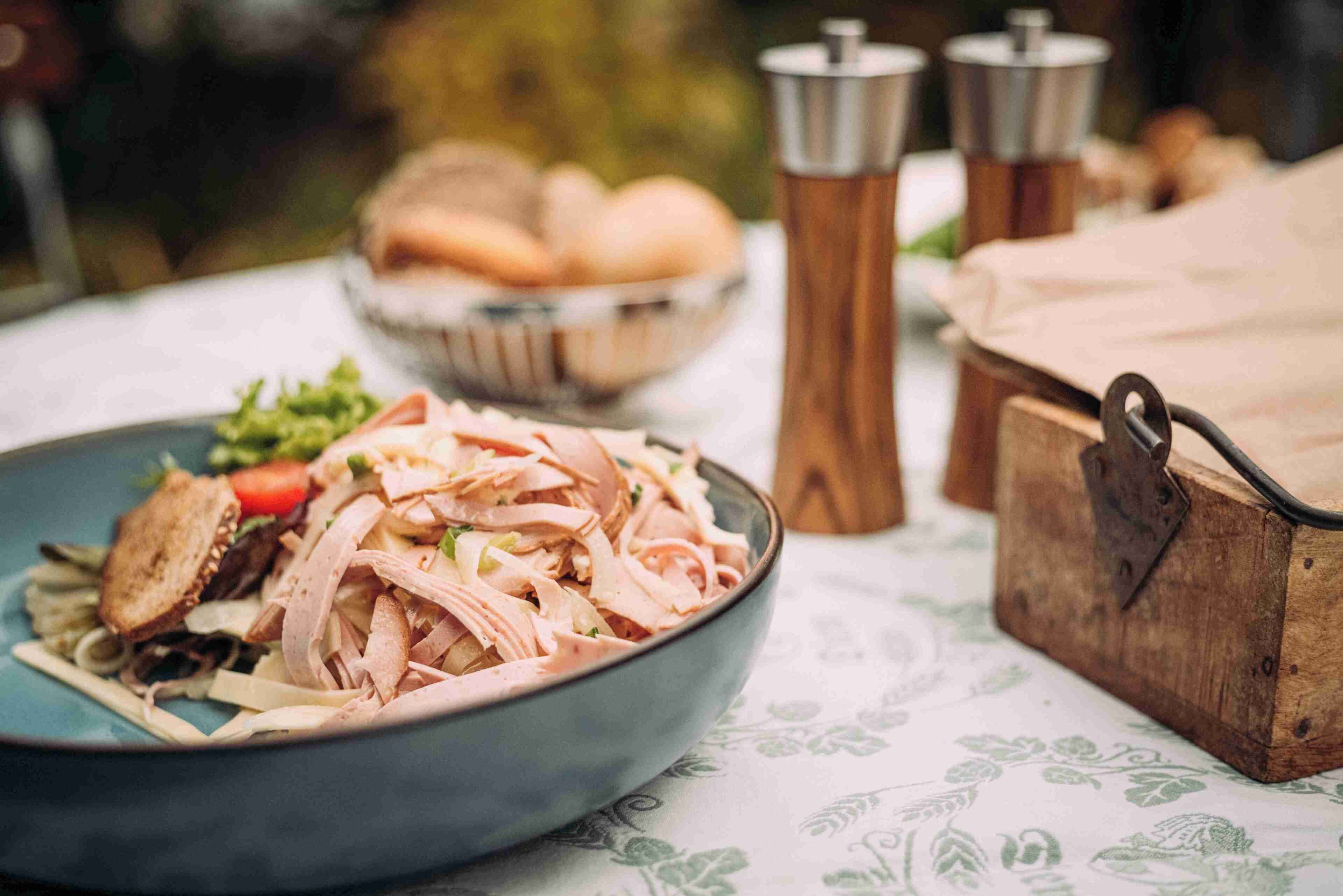 Eine Mahlzeit mit geschnittenem Fleisch und Gemüse, eine Brotschale und eine Holzkiste auf einem Tisch mit gemustertem Tischläufer.
