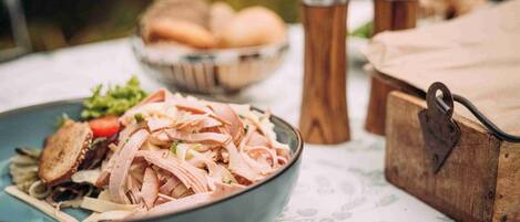 A meal with sliced meat and vegetables, a bowl of bread, and a wooden box on a table with a patterned tablecloth.