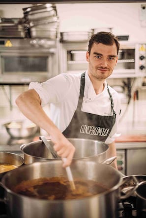 Un chef dans une cuisine professionnelle, avec des casseroles en acier inoxydable et un tablier blanc.