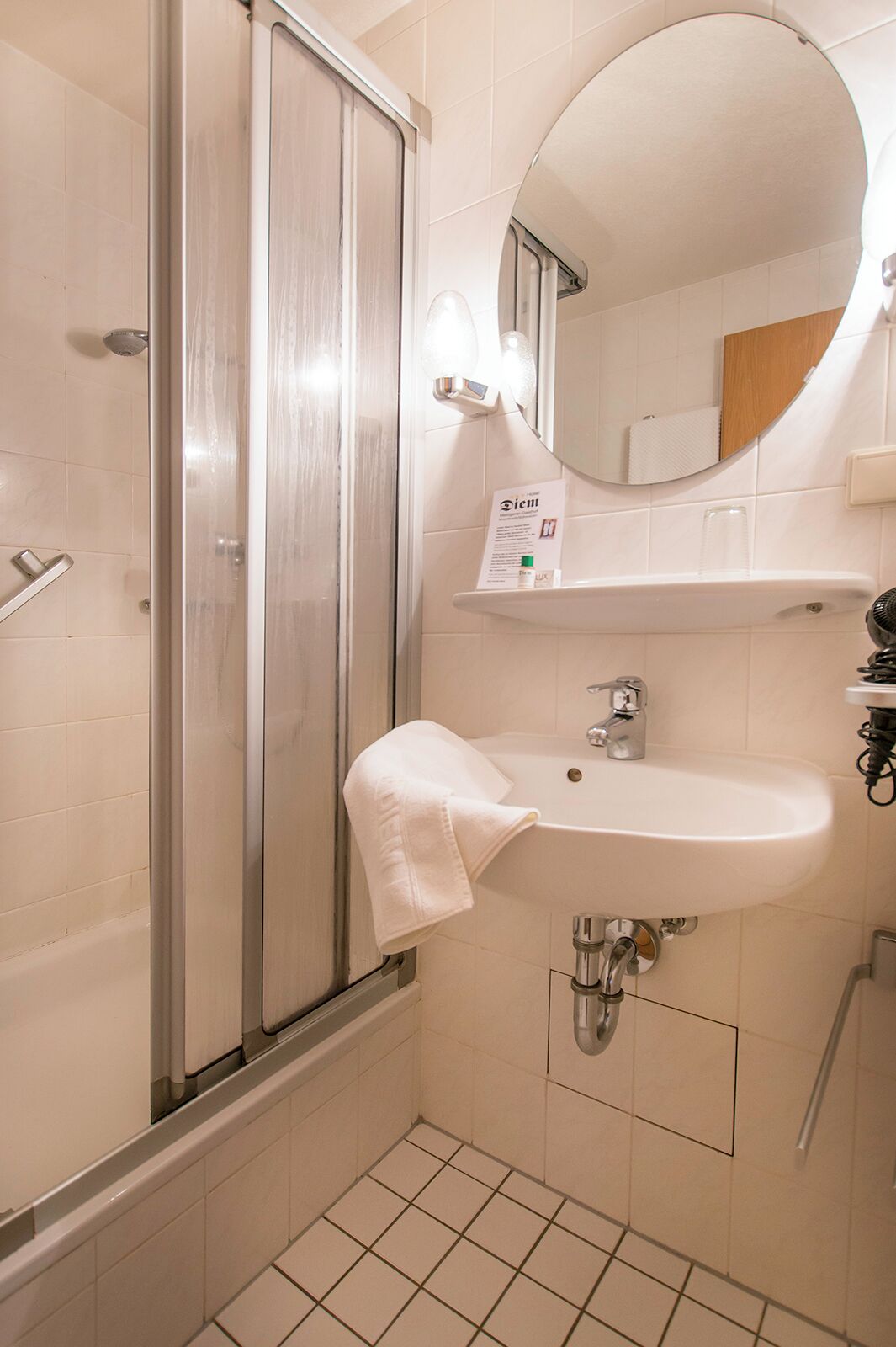 A bathroom with a glass shower enclosure, a sink with a mirror above it, and a white towel hanging on the shower door.