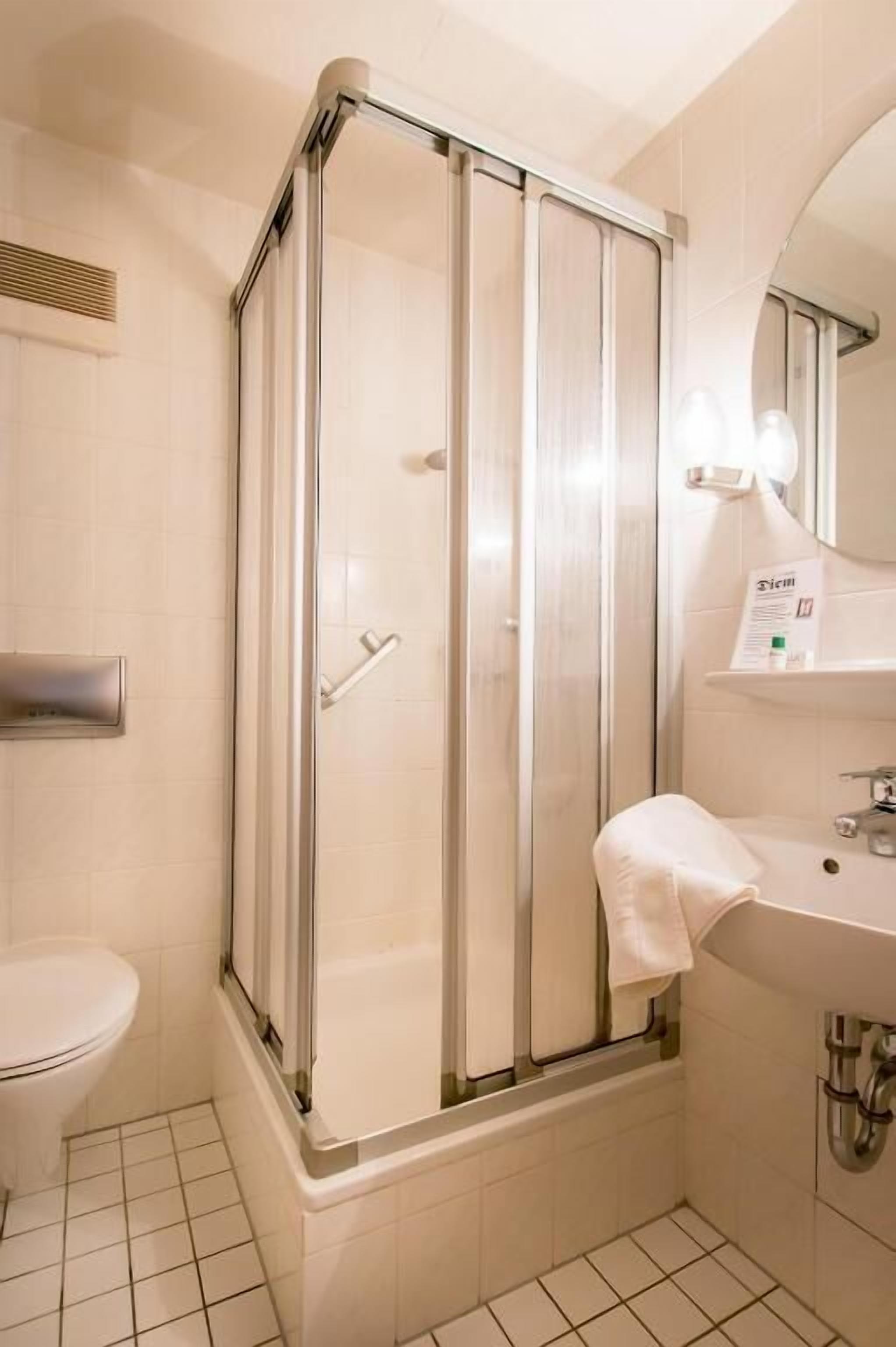 Un baño con ducha envuelta en vidrio, un inodoro y un lavamanos con una toalla.