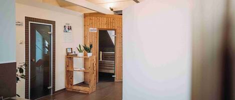 Zona de recepción con puerta de vidrio, mostrador de madera, planta en maceta y escalera que sube a un nivel superior.