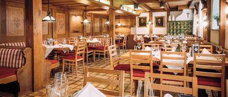 Un restaurante con muebles de madera, mesas dispuestas con manteles blancos y lámparas colgantes.