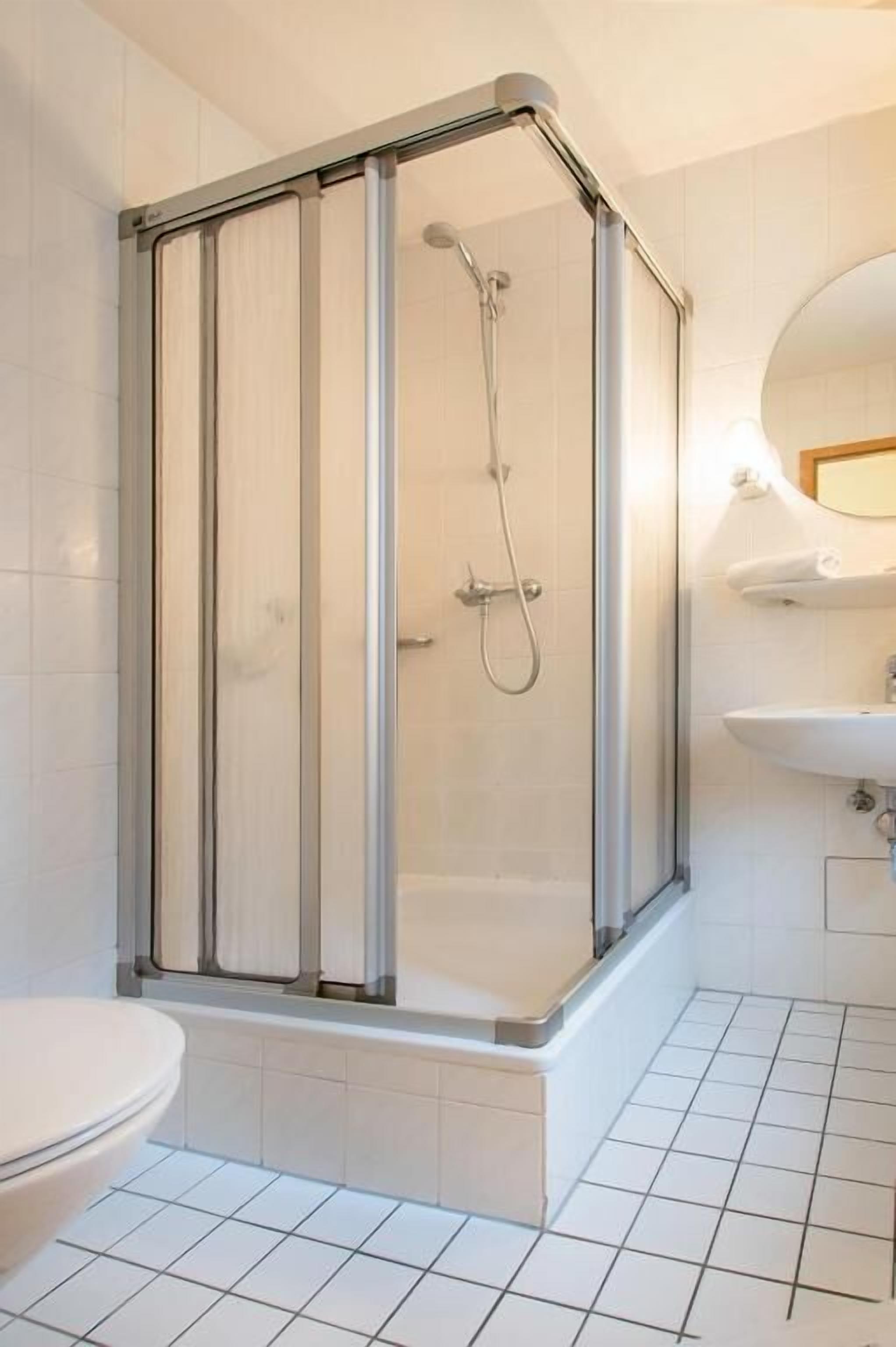 Een douche in hoekopstelling met een glazen deur, een wit toilet en een wastafel met spiegel.