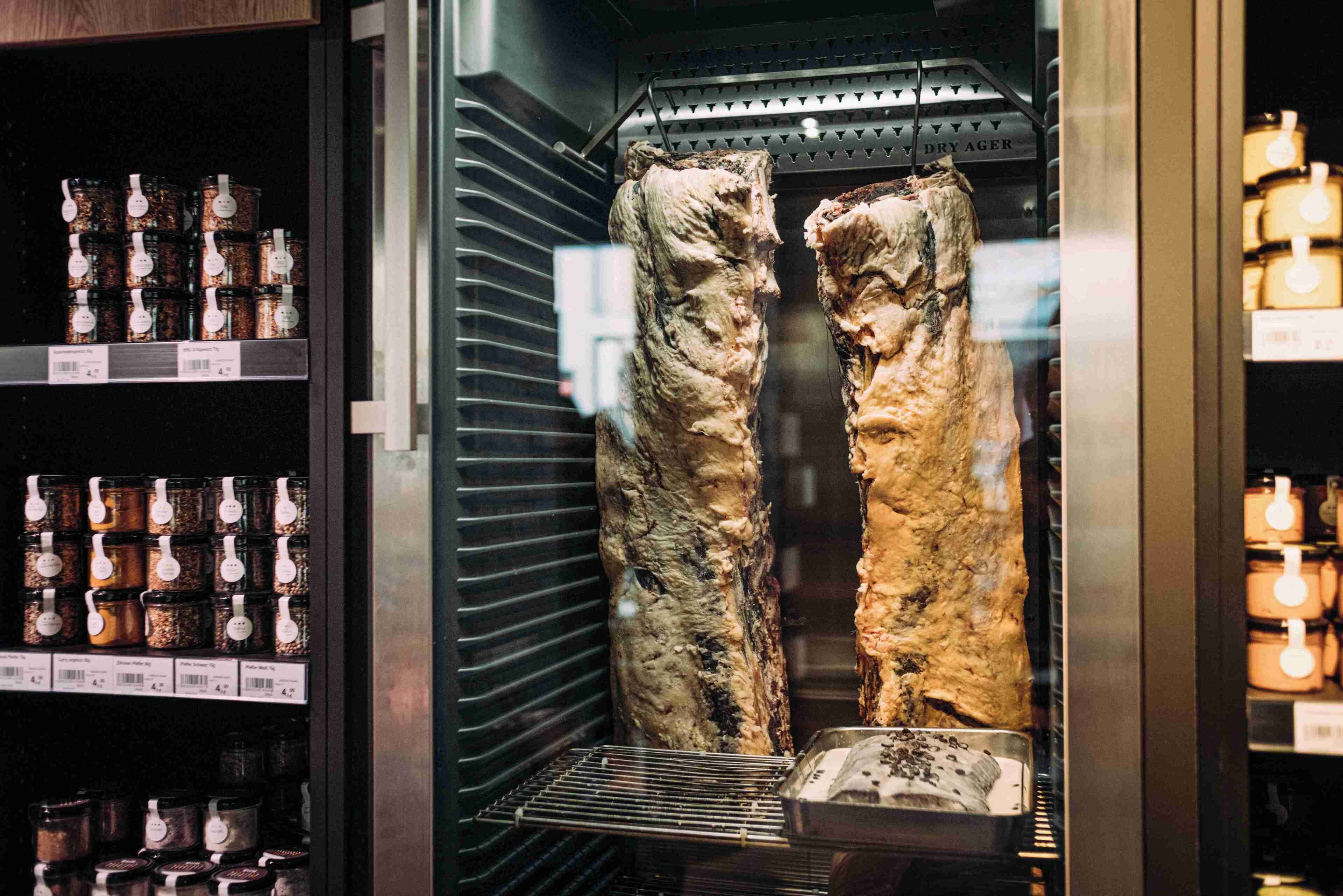 A meat display with hanging cuts and spice jars in the background.