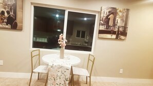 Uma sala de jantar com uma mesa redonda, duas cadeiras, um vaso com flores e dois quadros na parede.