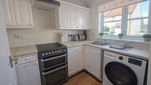 A compact kitchen with white cabinets, a built-in oven, a washing machine, and a window with a view of buildings. - Newly Renovated 2-Bed House w/ Parking – Sleeps 5 Near Shaftesbury Town (Shaftesbury)