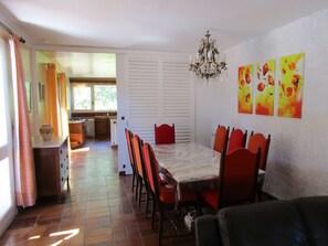 Un comedor con una mesa, sillas y una araña. Hay tres cuadros en la pared.