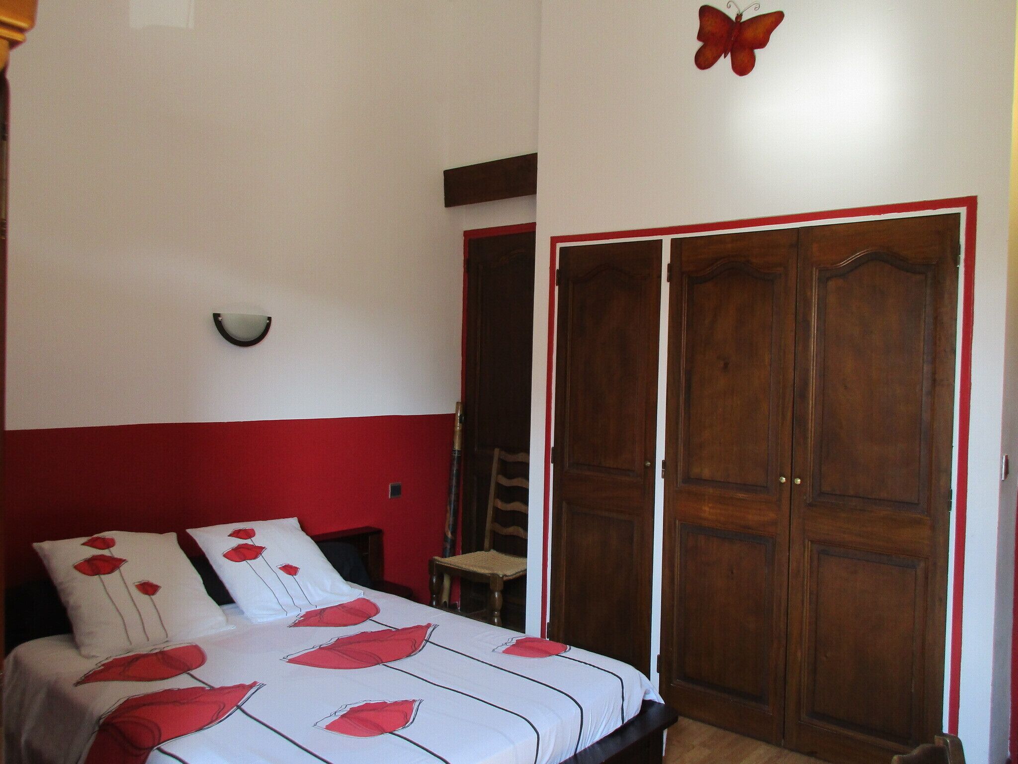 A bedroom with a bed, a wooden wardrobe, a chair, and a wall-mounted light fixture.