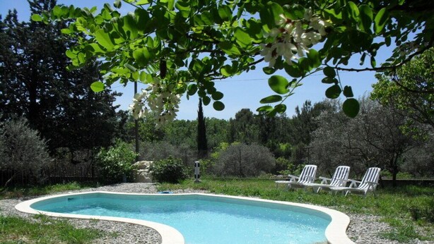 A swimming pool with a curved edge, surrounded by gravel, with trees and a fence in the background. - Spacious family villa with pool in the heart of green Provence, 4 bedrooms (Saint-Maximin-la-Sainte-Baume)