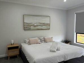 Un dormitorio con cama, mesita de noche, un cuadro colgado en la pared y ventana.