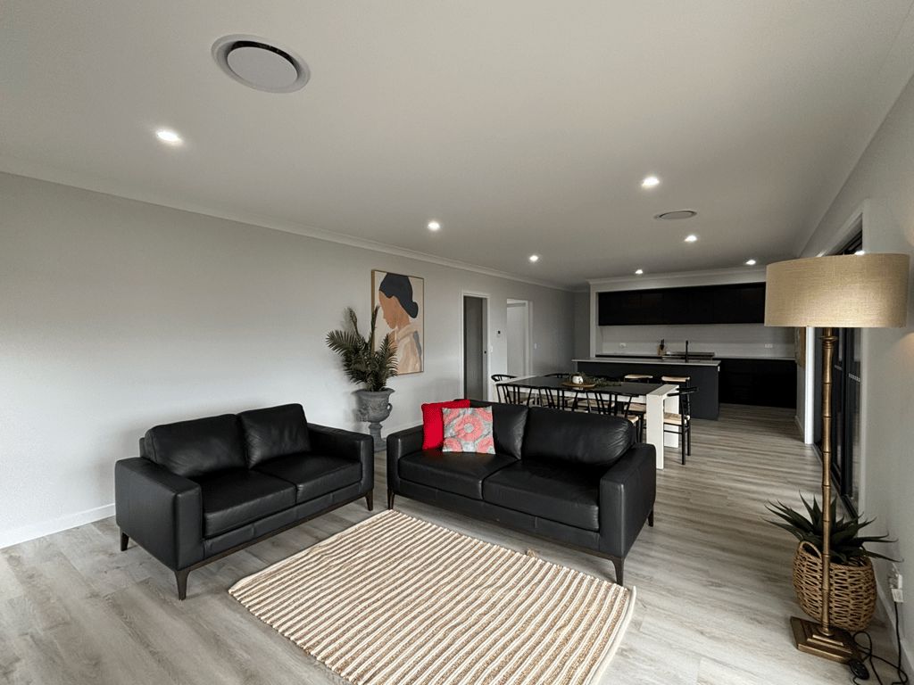 A modern living room with a black leather sofa, a dining table, and a kitchen in the background.