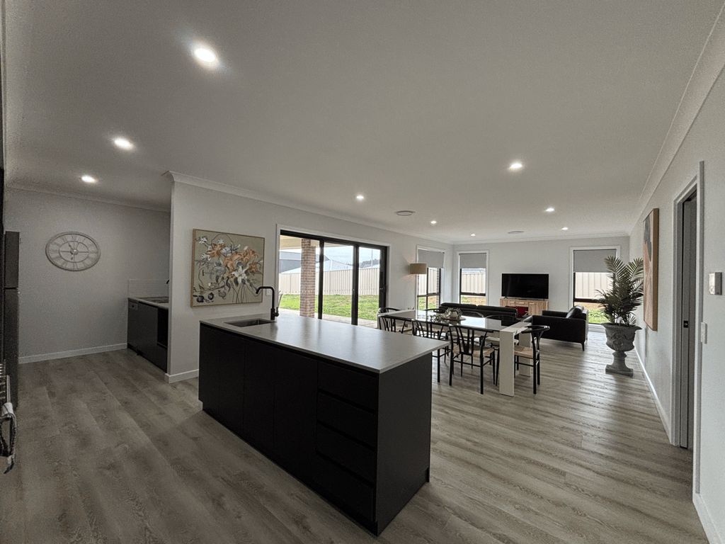 A modern kitchen with a central island, dining area with chairs, and a large window.