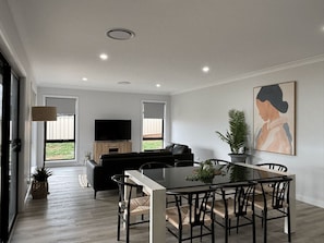 A modern living room with a black sofa, a dining table with chairs, a flat-screen TV, and a large abstract painting on the wall. - Wyoming Getaway Two - Sleeps 8 (Wagga Wagga)