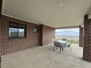 An outdoor patio area with a brick wall, a window, and a table with chairs. - Wyoming Getaway Two - Sleeps 8 (Wagga Wagga)