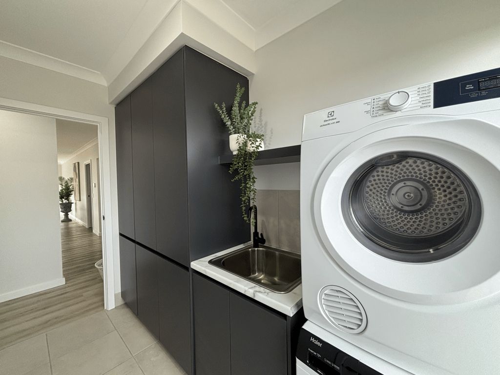 A modern kitchen with a built-in washer and dryer, dark cabinetry, and a small sink.