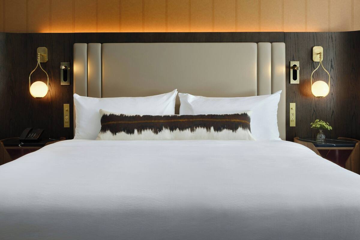 A hotel room with a large bed, two bedside tables, a wall-mounted phone, and two wall sconces.