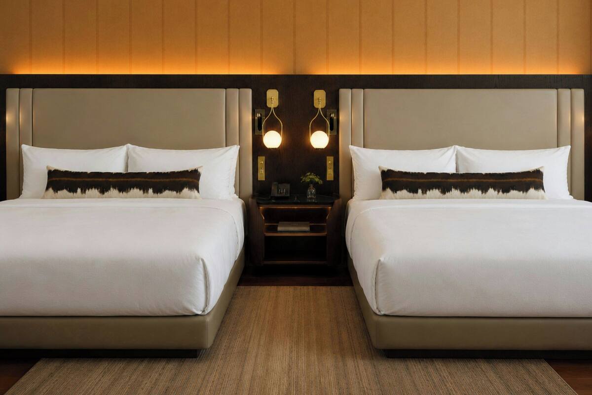 A hotel room with two beds, a nightstand, and wall-mounted lighting.