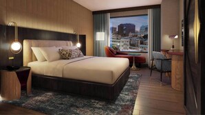 A hotel room with a large bed, a desk, a chair, and a view of the cityscape. - Hotel Trinity, Autograph Collection (Austin)