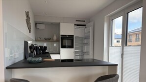 A modern kitchen with a central island, two bar stools, a built-in oven, and a large window. - "Baltic Sea happiness"... The sound of the sea included! (Dahme)