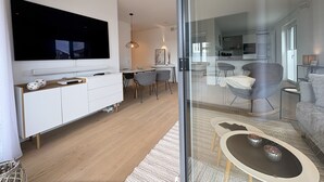 A modern living room with a large flat-screen TV, a dining area, and a kitchen visible through a glass partition. - "Baltic Sea happiness"... The sound of the sea included! (Dahme)