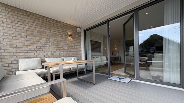 A modern outdoor living area with a brick wall, a wooden deck, and a glass door leading to an interior space. - "Baltic Sea happiness"... The sound of the sea included! (Dahme)