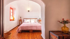 A bedroom with a wooden floor, a bed with a pink bedspread, a vase with flowers, and a wooden chest of drawers. - Villa del Conte | Exclusive Villa with Private Pool & Panoramic Garden (Alghero)