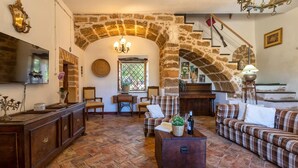 A cozy living room with a stone archway, a fireplace, a television, and a staircase. - Villa del Conte | Exclusive Villa with Private Pool & Panoramic Garden (Alghero)