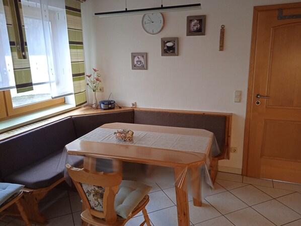 A dining area with a wooden table, chairs, a bench, a clock, and framed pictures on the wall.