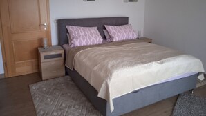 A bedroom with a bed, nightstands, a wooden door, and a wall-mounted shelf unit.