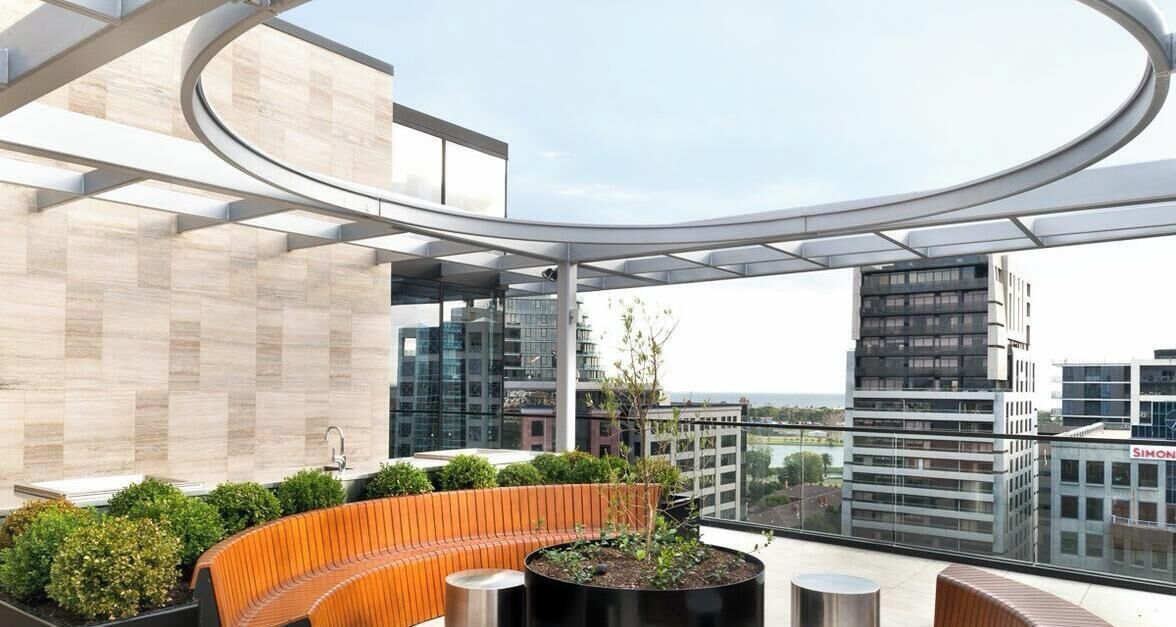 A rooftop terrace with a curved glass structure, seating areas, and a view of surrounding buildings.